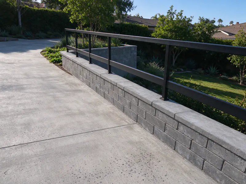 Driveway beside a short retaining wall with a metal guard along the top of the drop