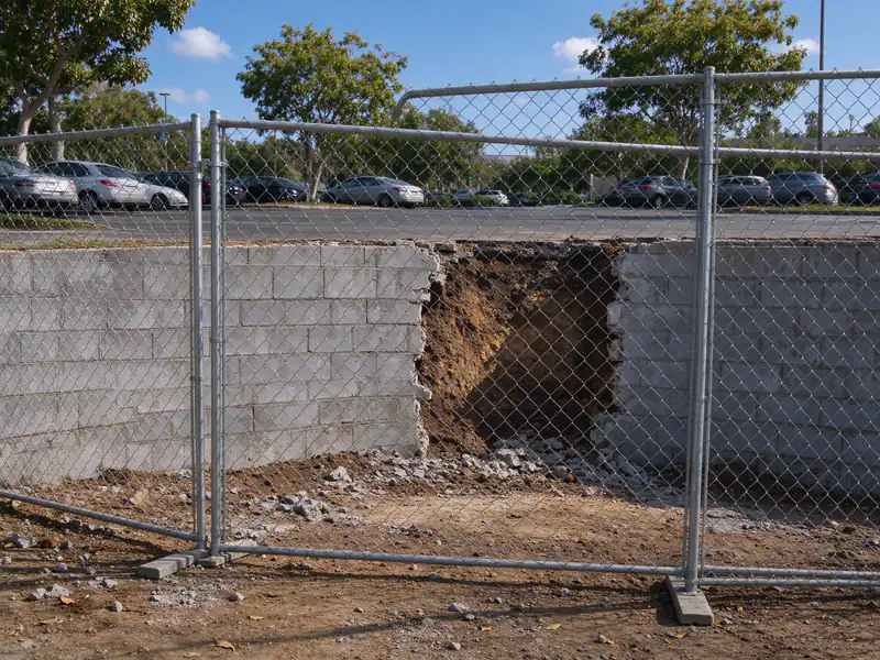 Section of a long retaining wall fenced off for rebuilding while the rest of the parking lot stays open